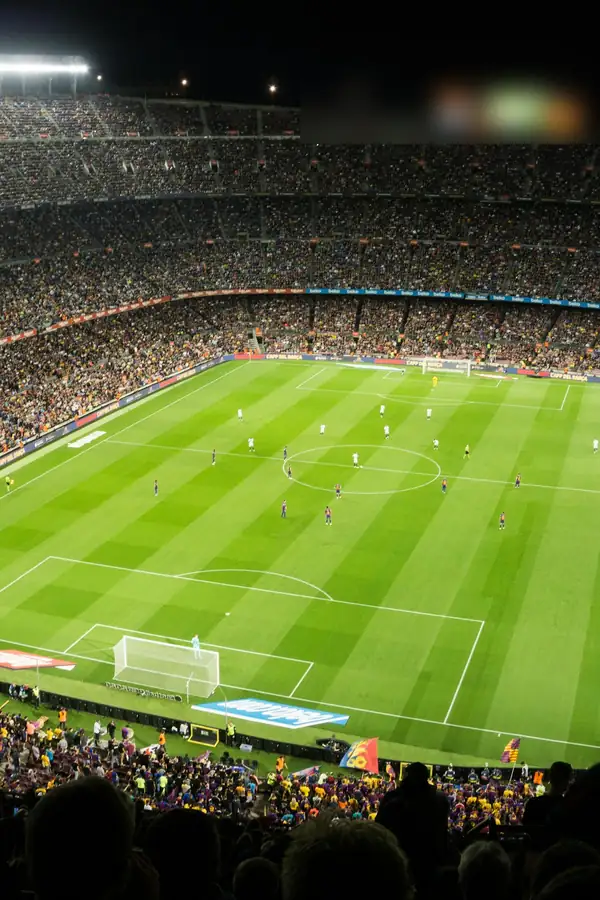 Estadio de fútbol lleno, de noche, con la cancha iluminada